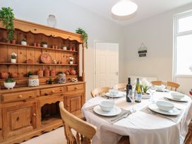 A dining room with a round table set for six and a wooden cabinet with jars and plants at 34 North Denes Road in Great Yarmouth