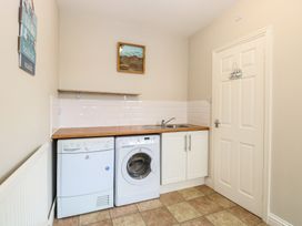 A utility room with a washing machine dryer under a wooden countertop and a sink near a closed door at 34 North Denes Road in Great Yarmouth