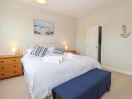 A bedroom with a double bed and striped pillows two bedside tables with lamps and a painting of a beach above the bed at 34 North Denes Road in Great Yarmouth