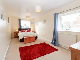 A bedroom with a bed with red pillows two windows blue curtains a wooden chest and a red rug at 34 North Denes Road Great Yarmouth