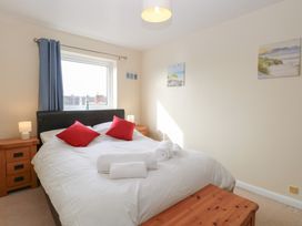 A bedroom with a double bed with red pillows and white towels on top two bedside tables with lamps a window with blue curtains and wall paintings at 34 North Denes Road in Great Yarmouth