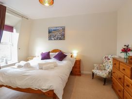 A bedroom with a wooden bed with white bedding and purple pillows wooden nightstand and dresser a floral armchair and a window at 34 North Denes Road in Great Yarmouth