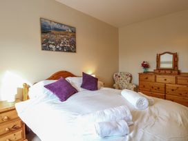 A bedroom with a bed with white sheets and purple pillows a wooden dresser with a mirror and a floral armchair at 34 North Denes Road in Great Yarmouth