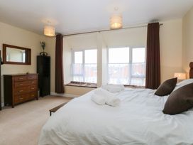 A bedroom with a bed white bed linens brown pillows towels wooden dresser mirror and two large windows with brown curtains at 34 North Denes Road in Great Yarmouth