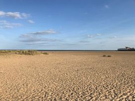 A sandy beach with sparse vegetation and a pier in the distance at 34 North Denes Road in Great Yarmouth