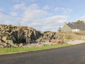 A wooden bench on gravel next to rocky terrain with a stone wall and a house in the background at Dunskey Way in Portpatrick