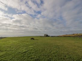 A large grassy field with a wooden picnic table and a distant stone building at Dunskey Way Portpatrick