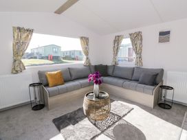 A living room with a gray sectional sofa, two black side tables, a round wicker coffee table with a vase of purple flowers and patterned curtains at Dunskey Way in Portpatrick