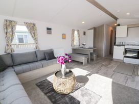 A living area with a gray sectional sofa a round wicker coffee table with flowers a dining table with bench seats and a kitchen with white cabinets and stove at Dunskey Way in Portpatrick