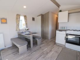 A dining area with a table set for four and benches next to a kitchen with a stove at Dunskey Way in Portpatrick