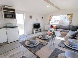 A dining table set with dishes and flowers in a living room with a gray sofa a TV and kitchen appliances at Dunskey Way in Portpatrick