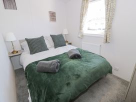 A bedroom with a double bed green blanket two rolled gray towels two bedside tables with lamps and a window with patterned curtains at Dunskey Way in Portpatrick