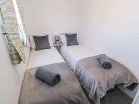 A bedroom with two single beds with gray blankets and pillows with a small table and lamp between them at Dunskey Way in Portpatrick