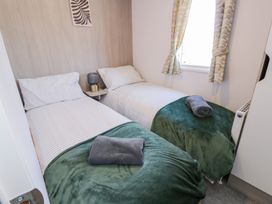 A small bedroom with two single beds green blankets and grey towels beside a window with patterned curtains at Dunskey Way in Portpatrick