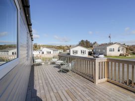 An outdoor wooden deck with chairs and a table overlooking houses and a car at Dunskey Way in Portpatrick