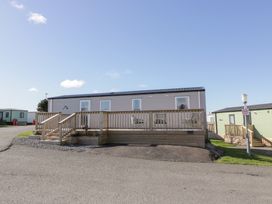 A mobile home with a wooden deck and outdoor chairs on a paved road at Dunskey Way in Portpatrick