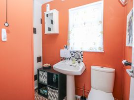 A bathroom with an orange wall a white sink and toilet a window with floral curtains and a black storage unit at 271 California Sands Estate California Norfolk