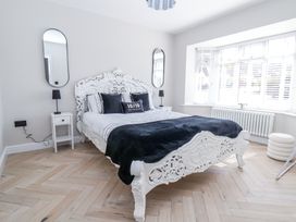 A bedroom with a carved white bed frame black pillows bedside tables with lamps and two oval mirrors near large windows at Ty Blodau near Prestatyn