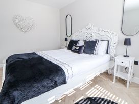 A bedroom with a white decorative bedframe black and white bedding two bedside tables with black lamps a heart-shaped wall decoration and two vertical mirrors at Ty Blodau near Prestatyn
