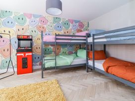 A bedroom with two bunk beds bedding in different colors and a red arcade game machine near a wall with smiley face wallpaper at Ty Blodau near Prestatyn