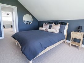 A bedroom with a bed with dark blue bedding and beige pillows a wooden nightstand with lamp and a round mirror on the wall at Ty Blodau near Prestatyn