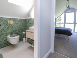 A bathroom with green tiles and a toilet next to a bedroom with a bed near large windows at Ty Blodau near Prestatyn