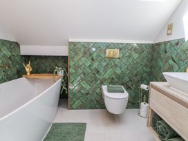 A bathroom with a white bathtub a wall-mounted toilet and a wooden vanity with towels at Ty Blodau near Prestatyn