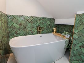 A bathroom with a white freestanding bathtub green tiled walls and a plant on the tub edge at Ty Blodau near Prestatyn