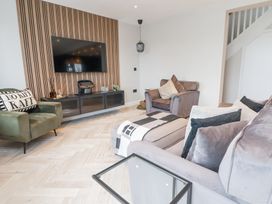 A living room with velvet armchairs a wall-mounted TV and a wooden slat panel at Ty Blodau near Prestatyn
