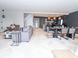 An open plan living room and dining area with grey sofas and chairs a dining table with chairs and hanging lamps at Ty Blodau near Prestatyn