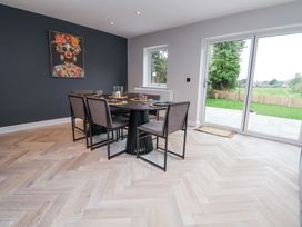 A dining area with a black table and six chairs near a window and glass doors overlooking a garden at Ty Blodau near Prestatyn