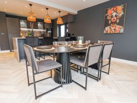 A dining room with a round table and six chairs and a kitchen area with three pendant lights and black cabinets at Ty Blodau near Prestatyn