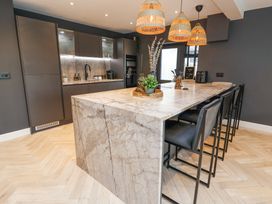 A kitchen with a marble island and black chairs under woven pendant lights at Ty Blodau near Prestatyn