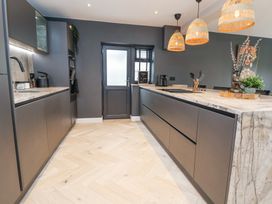 A modern kitchen with dark cabinets a marble countertop wooden floor and pendant lights at Ty Blodau near Prestatyn