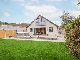A backyard with green grass patio and a modern house with large windows at Ty Blodau near Prestatyn