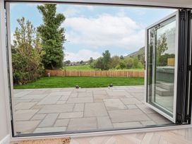 A garden with a stone patio grass lawn and wooden fence viewed through open glass doors at Ty Blodau near Prestatyn