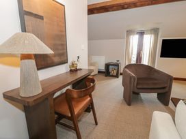 A living room with a wooden desk and chair a brown armchair and a window with curtains at Y Granar in Conwy