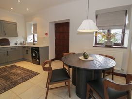 A kitchen area with gray cabinets a black washing machine a round wooden dining table with four chairs and a hanging light at Y Granar in Conwy