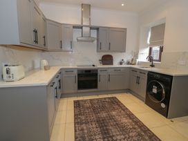A kitchen with grey cabinets marble countertops a black washing machine and a patterned rug at Y Granar in Conwy