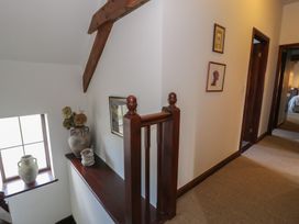 A hallway with framed pictures on the wall a wooden railing and pottery on a ledge near a window at Y Granar in Conwy