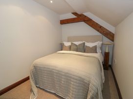 A bedroom with a bed under a wooden ceiling beam and two bedside lamps at Y Granar in Conwy