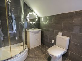 A bathroom with a shower enclosure a white sink with cabinet a round illuminated mirror and a toilet at Y Granar in Conwy