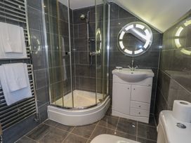 A bathroom with a glass shower enclosure white sink cabinet round mirror towel rack and toilet at Y Granar in Conwy