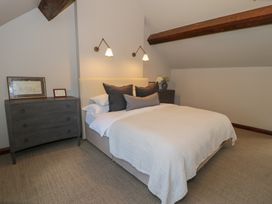 A bedroom with a bed with white and grey pillows two grey dressers and wooden beams on the ceiling at Y Granar in Conwy
