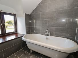 A bathroom with a white freestanding bathtub and tiled gray walls and floor next to a window with a wooden sill at Y Granar in Conwy