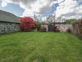 A garden with green grass a stone building a brick wall with a wooden door and various trees and shrubs at Y Granar in Conwy
