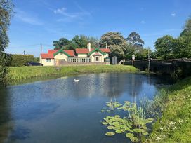A pond with water lilies and a swan in front of a house with red roofs and green trim near a stone bridge at Hafod Lodge in Hensol near Pontyclun