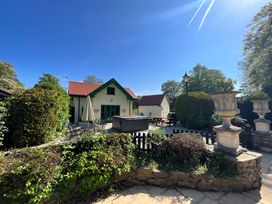An outdoor patio area with tables chairs a hot tub garden urns and a house with a red roof at Hafod Lodge in Hensol near Pontyclun