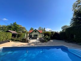An outdoor swimming pool with a paved patio area in front of a small house surrounded by trees and shrubs at Hafod Lodge in Hensol near Pontyclun