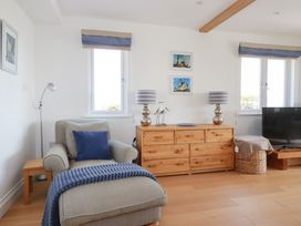 A living room with a gray armchair blue cushion and blanket wooden dresser lamps and a television at The Old Harbour Masters House in Fowey